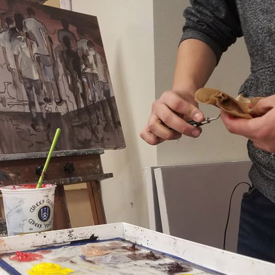 Student clenaing his pallete knife with a painting in the background