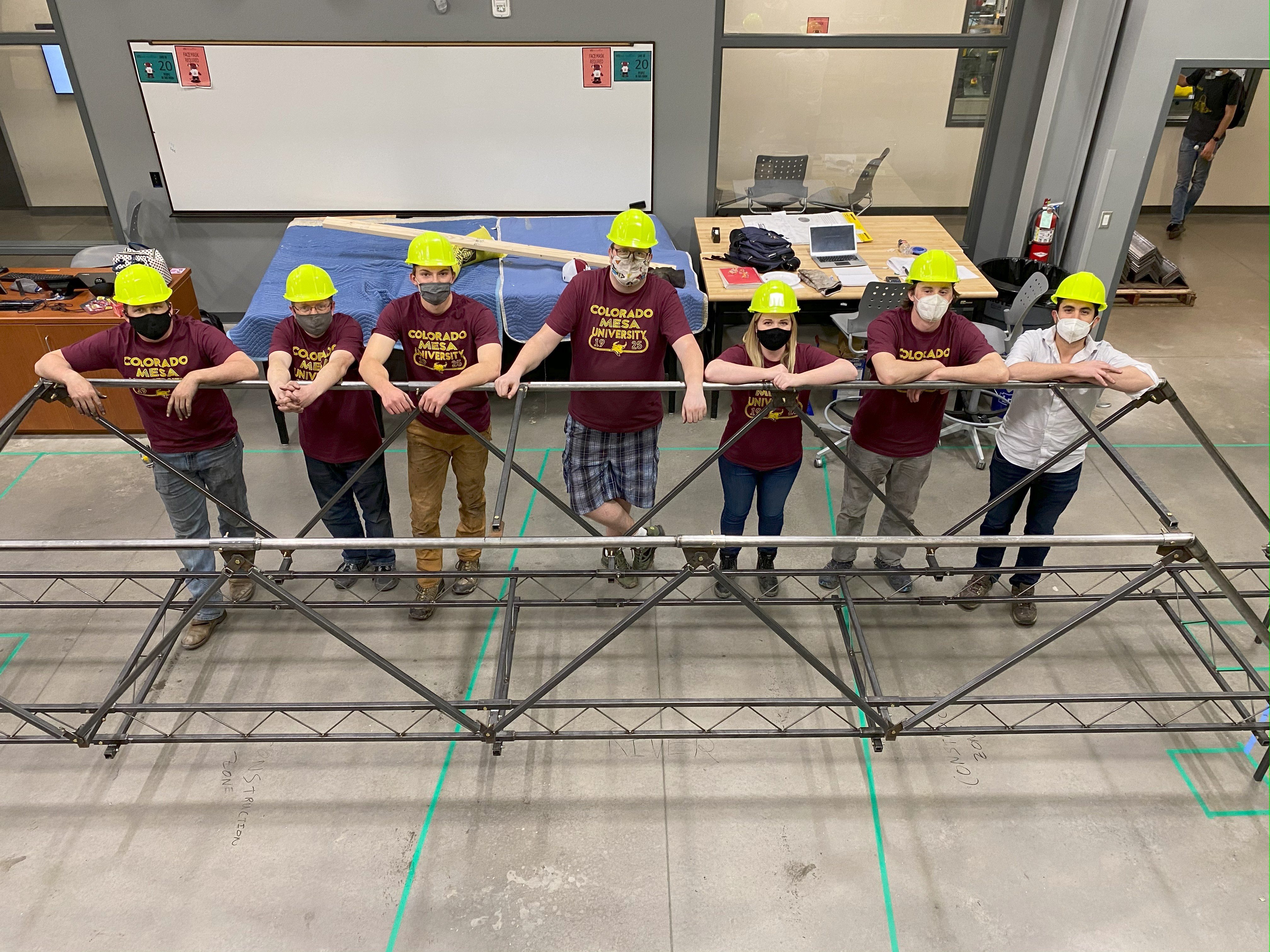 Civil club members with hard hats on standing next to the steel bridge they fabricated.