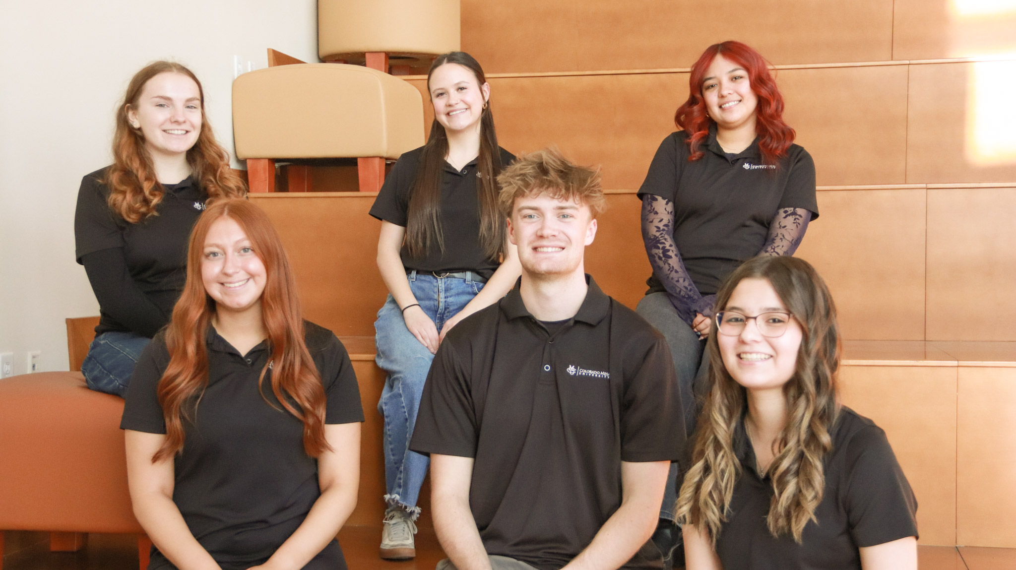 six students sitting in two rows and smiling at camera