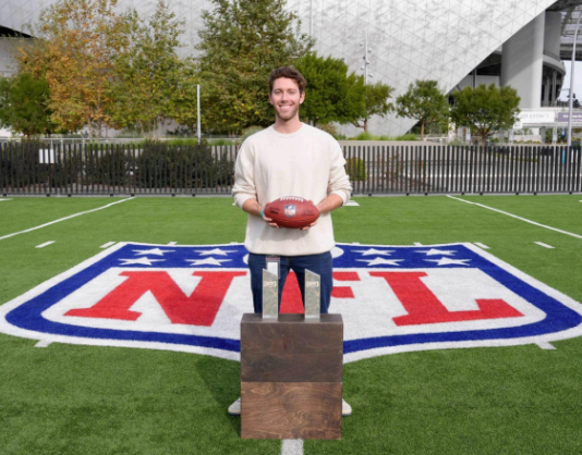 Student holding a football standing in front of an NFL logo on a football field.
