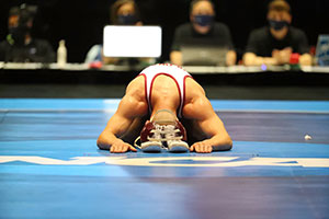 wrestler kneels on mat with head gear and shoes in front of him