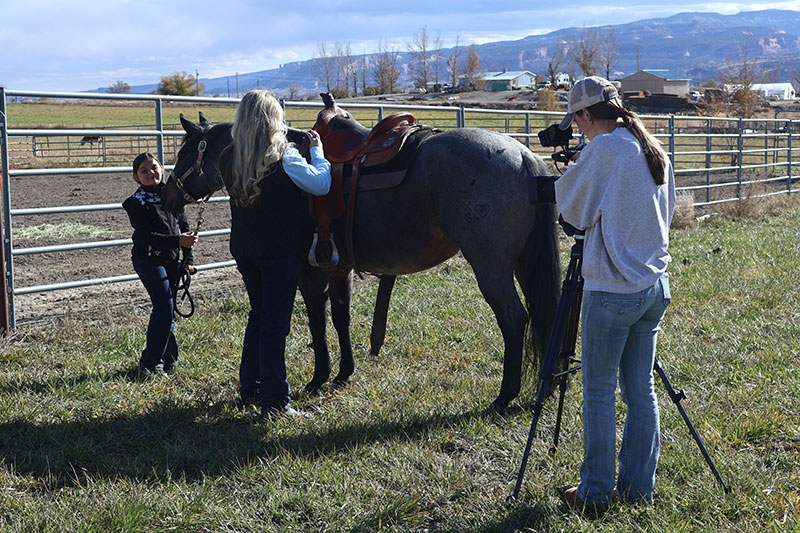 CMU Communications Studies Instructor Tara Carleo raises performance quarter horses at the XS Heart Ranch West Division. She is pictured here with her daughter, Lena, who is holding the horse, and is being filmed by CMU student Jordan Neifert. Photo credit: Laurena Davis