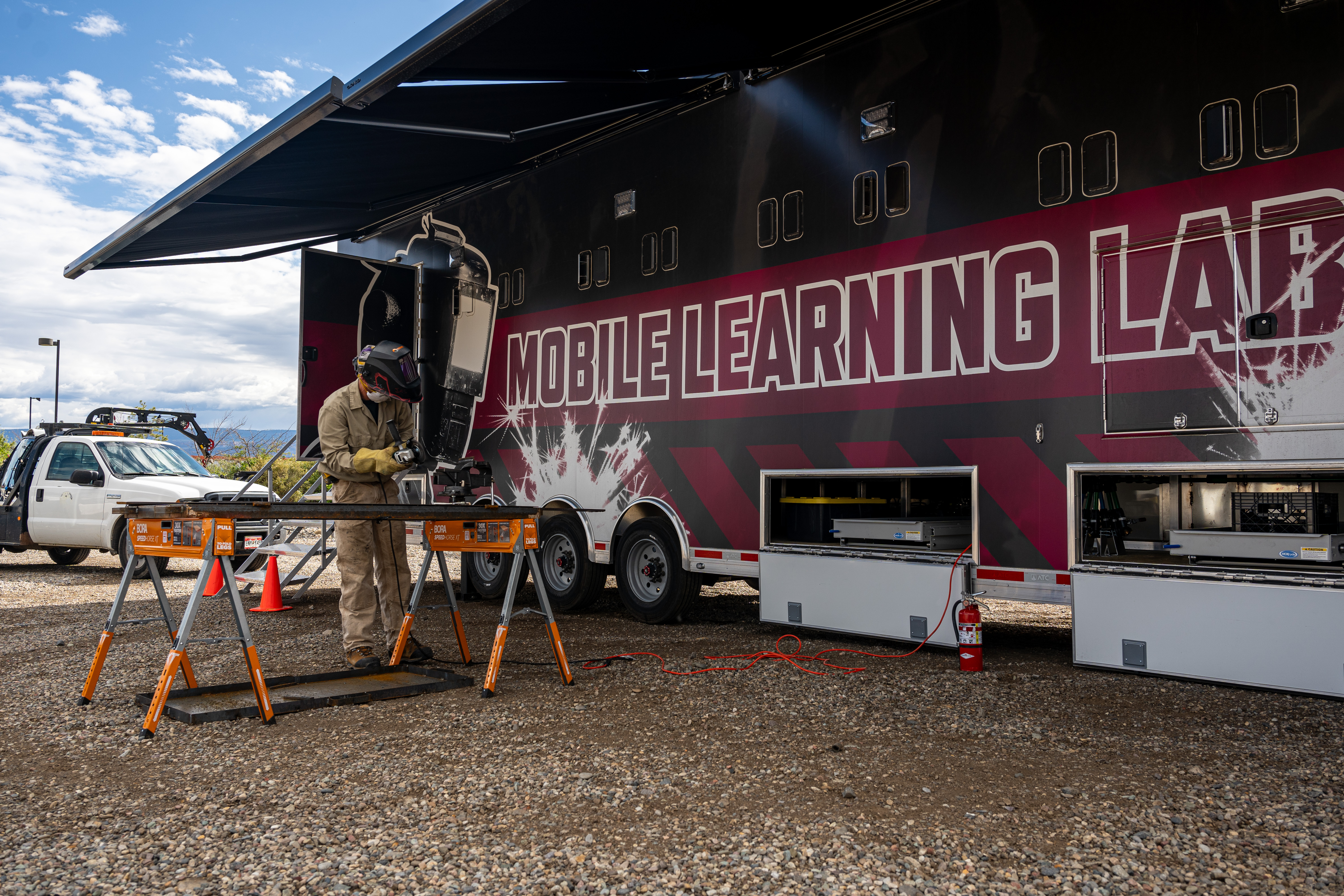 A CMU Tech Mobile Learning Lab is set up at a local business, with an employee participating in hands-on welding training outside the mobile facility.